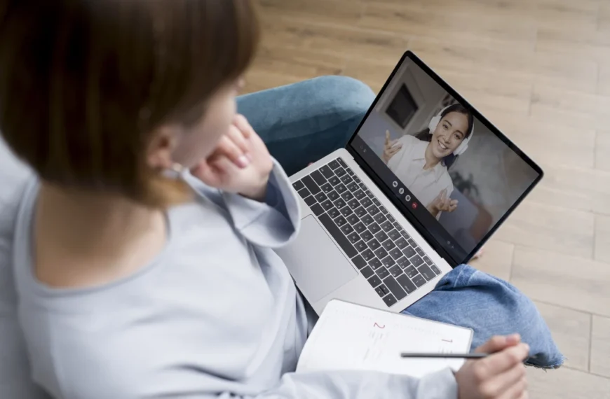 Persona sentada en un sofá tomando notas mientras realiza una videollamada en una computadora portátil, demostrando cómo atraer a tu paciente ideal con una web diseñada para psicólogos puede facilitar conexiones profesionales y efectivas en terapia online.