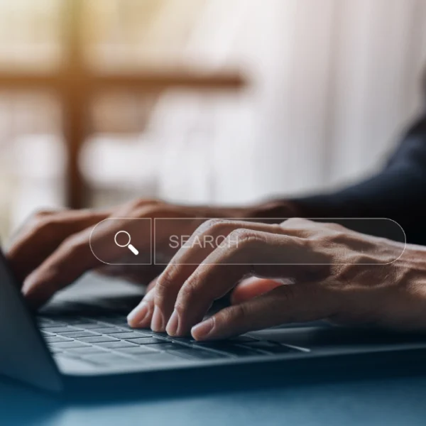 Primer plano de las manos de una persona escribiendo en un teclado portátil con una barra de búsqueda virtual superpuesta, resaltando el Diseño Web que inspira Confianza.