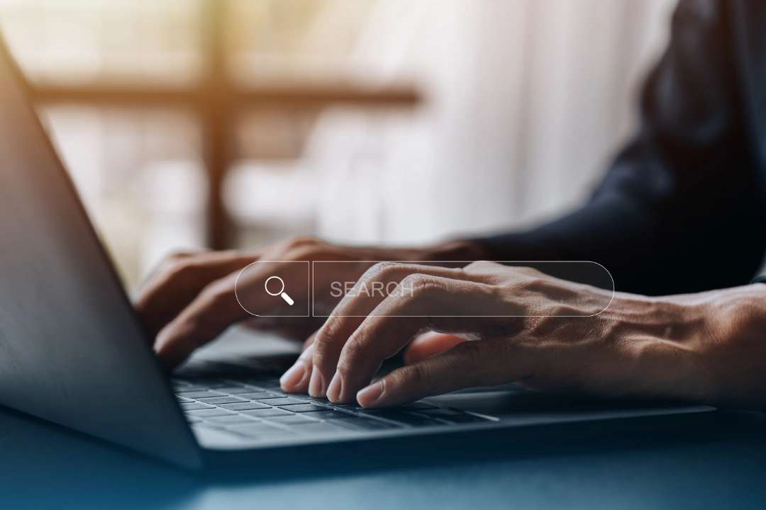 Primer plano de las manos de una persona escribiendo en un teclado portátil con una barra de búsqueda virtual superpuesta, resaltando el Diseño Web que inspira Confianza.