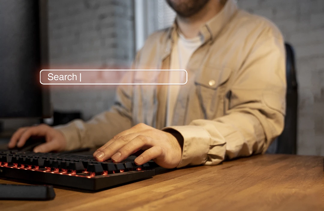Una persona con una camisa beige se sienta en un escritorio usando un teclado, con un gráfico de barra de búsqueda digital superpuesto cerca de sus manos, lo que ilustra el diseño web centrado en el paciente.