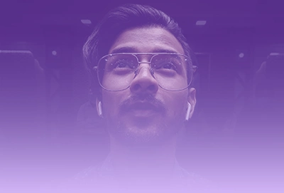 img-ter-ind-5d Una persona con gafas y auriculares mira hacia arriba, con un degradado violeta superpuesto a la imagen, perfecto para mejorar su página de destino e impulsar la conversión del sitio web.