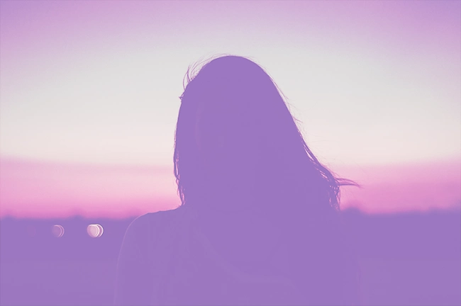 img-ter-ind-5f Silueta de una persona con cabello largo contra un cielo degradado de color púrpura y rosa al atardecer, como si capturara la belleza tranquila de sus momentos finales antes de aterrizar.